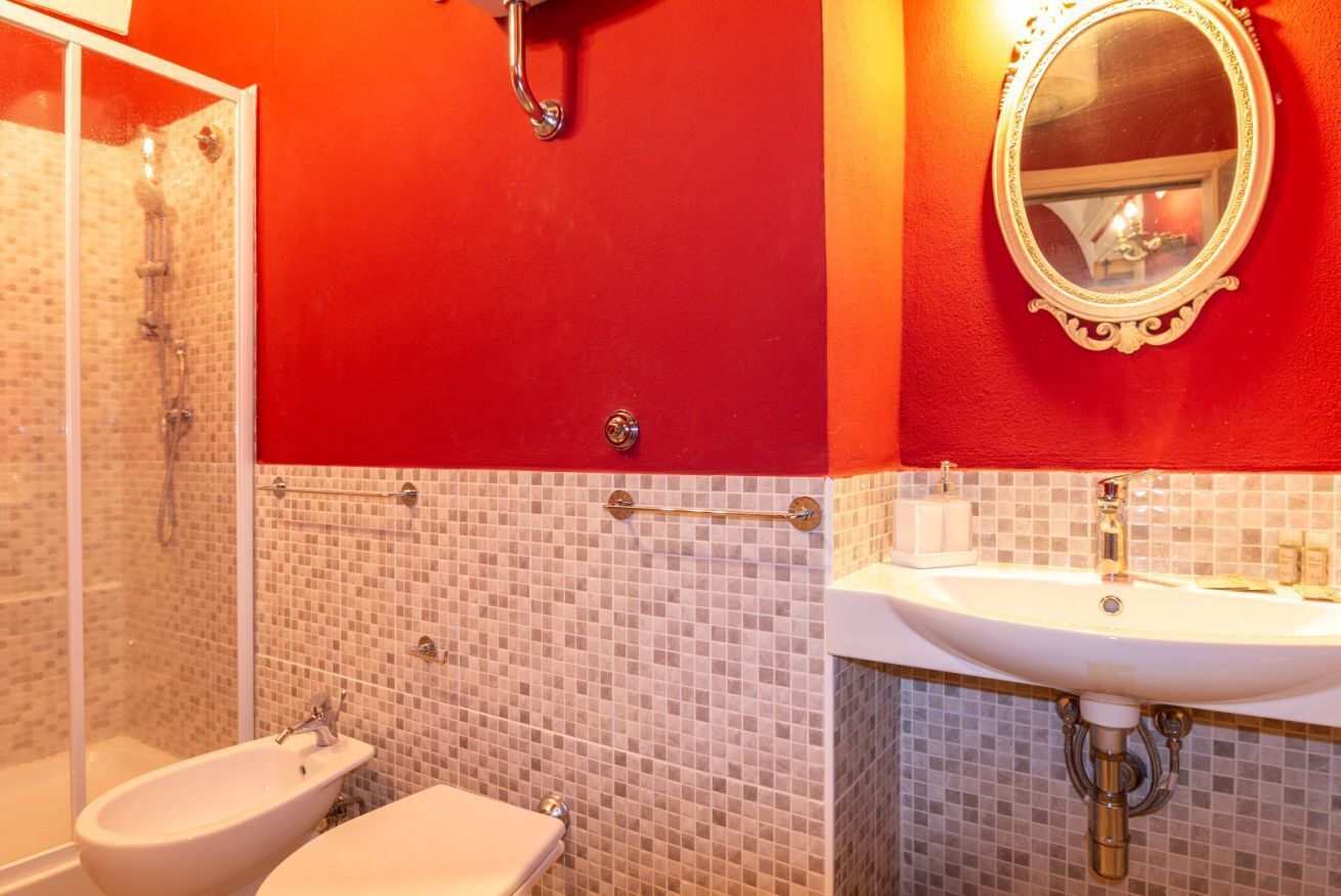 Une salle de bain équipée d’une douche, d’un bidet et d’un lavabo, avec des carreaux de mosaïque et un mur d’accent rouge.
