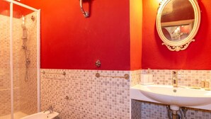 Een badkamer met douche, toiletgerei en wastafel, voorzien van mozaïektegels en een rode accentmuur.