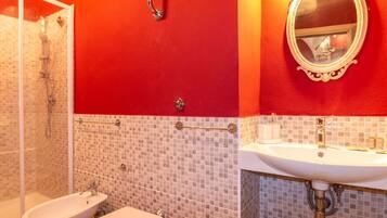 Une salle de bain équipée d’une douche, d’un bidet et d’un lavabo, avec des carreaux de mosaïque et un mur d’accent rouge.