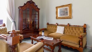Een klassieke kamer met een houten kast, een bank, een bijzettafeltje en een ingelijste foto aan de muur.