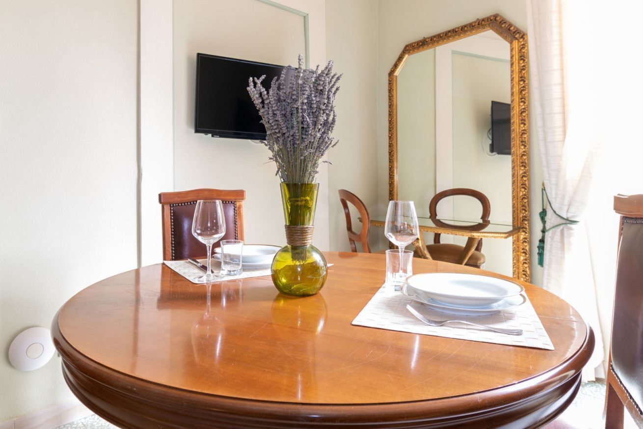 Une table à manger agrémentée d’un vase de lavande, un téléviseur à écran plat fixé au mur et un grand miroir.