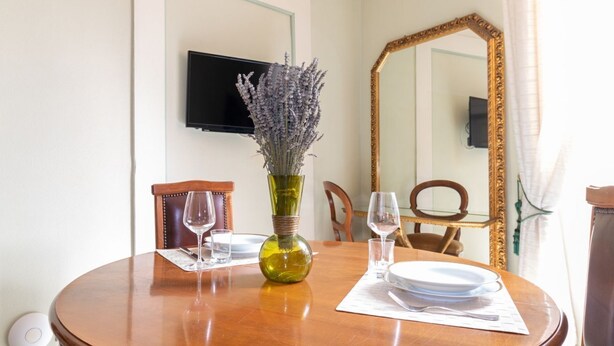 Een eettafel met een vaas lavendel, een flatscreen televisie aan de muur en een grote spiegel.