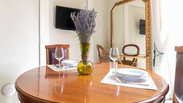 Une table à manger agrémentée d’un vase de lavande, un téléviseur à écran plat fixé au mur et un grand miroir.