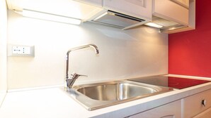 Een keuken met een RVS-gootsteen, witte kasten en een rode accentmuur.