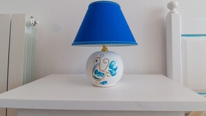A white bedside table with a blue lampshade and a decorative ceramic lamp base. - Cocco e Dessì Home- Mattia (ORISTANO)