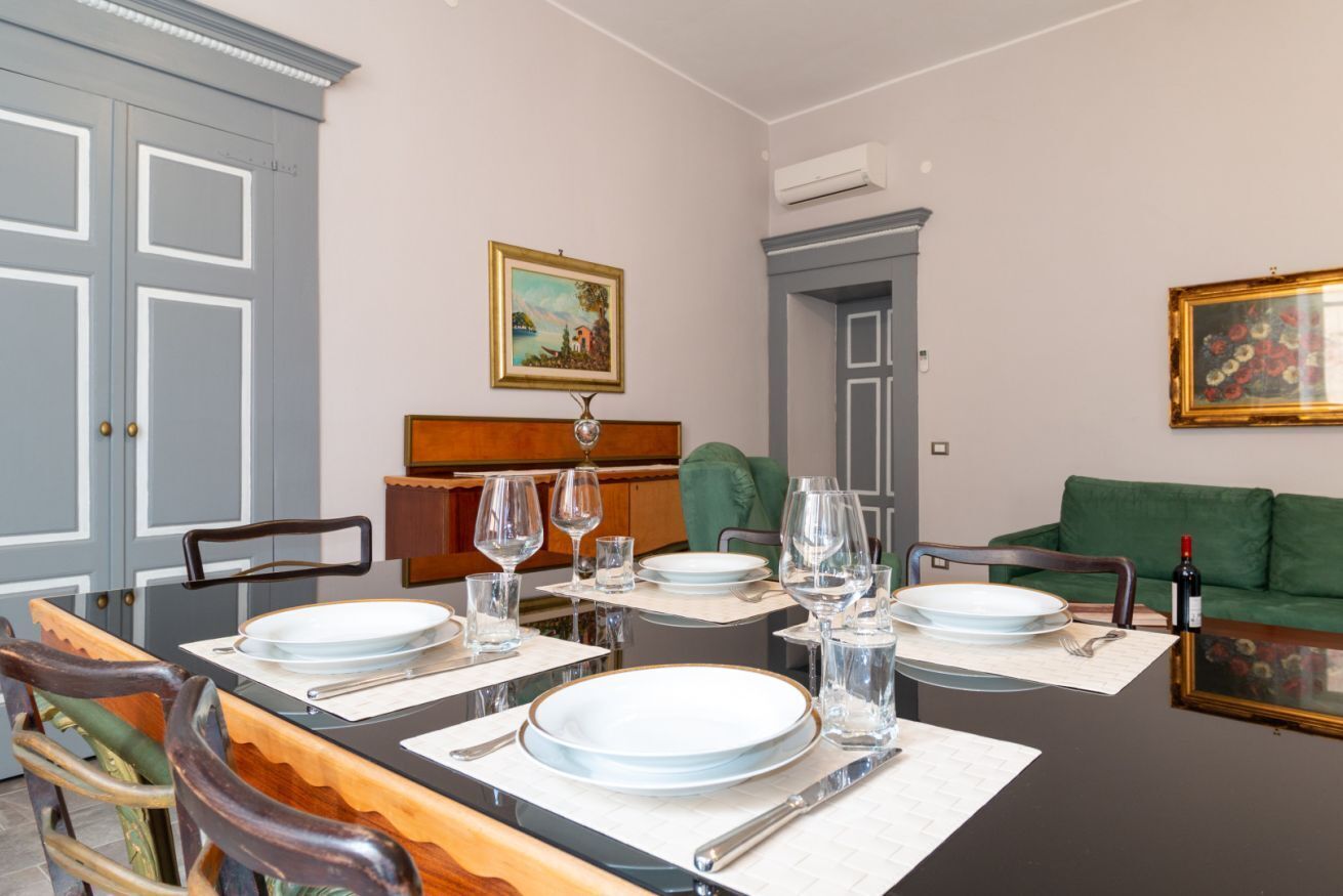 A dining area with a table set for four, chairs, a green sofa, and a painting on the wall.