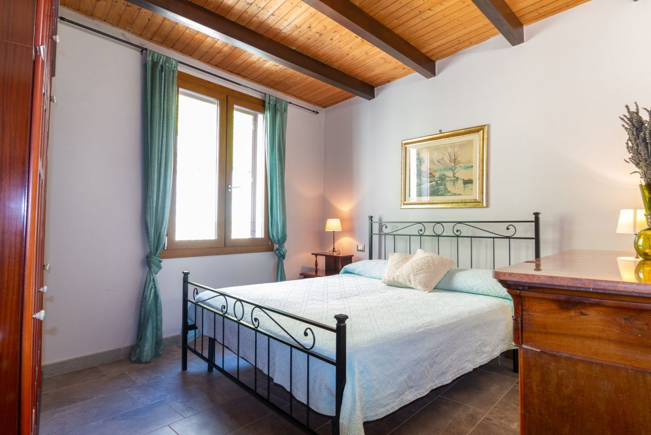 Ein Schlafzimmer mit Bett, Nachttisch, Lampe, einem Gemälde und einer Holzkommode.