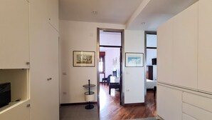 A hallway with a wooden floor, white walls, and a door leading to a room with a bed and a desk. There are framed pictures on the walls. - Casa D'Amato - Salerno (Salerno)