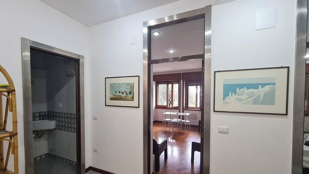 A hallway with a bathroom on the left, a dining area with chairs and a table in the center, and a framed picture on the right wall. - Casa D'Amato - Salerno (Salerno)