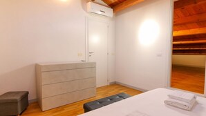 Una camera da letto con un letto, una cassettiera, una panca e una porta.