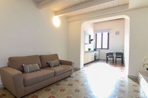 Uma sala de estar com um sofá, um espaço de refeições com mesa e cadeiras, e uma cozinha ao fundo.