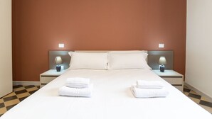 Quarto de hotel com uma cama grande, duas mesas de cabeceira com luminárias e um padrão de piso xadrez.