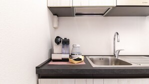 Una cucina moderna con lavandino in acciaio inossidabile, macchina per il caffè e bollitore sul piano di lavoro.