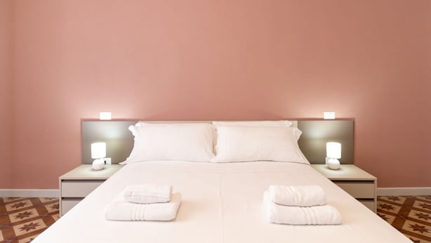 Una camera d'albergo con un letto, due comodini con lampade e due asciugamani piegati sul letto.