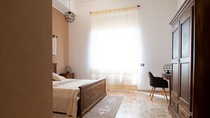 A bedroom with a bed, a chair, a wardrobe, and a window with curtains. - Cocco e Dessì Home- Angelica (ORISTANO)
