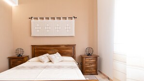 A bedroom with a wooden bed, two bedside tables with globe lamps, a wall-mounted curtain, and a patterned bedspread. - Cocco e Dessì Home- Angelica (ORISTANO)