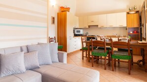 Een woonkamer met een bank, eettafel, stoelen en een keuken met kasten en een magnetron.