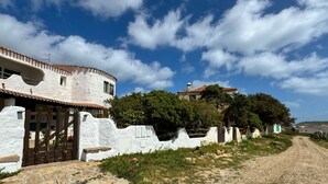 A white building with a wooden gate, a stone wall, and a clear blue sky with clouds. - La Casa Del Sole- Luxury home (San Giovanni di Sinis)