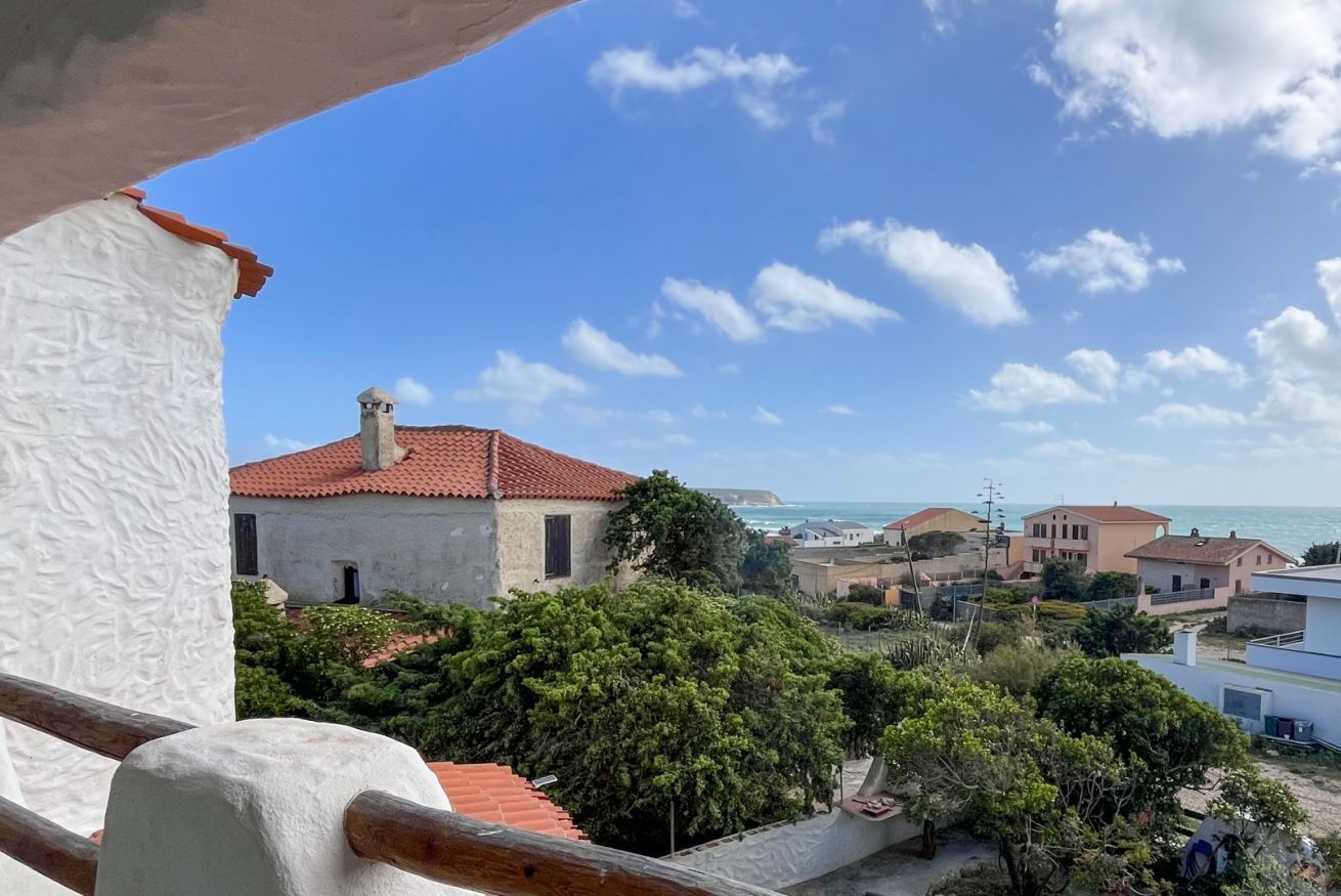 A coastal residential area with a view of the sea, houses with red-tiled roofs, and lush greenery.