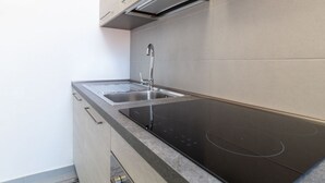 Una cucina moderna con lavello in acciaio inossidabile, piano cottura a induzione nero e mobili di colore chiaro.