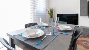 Un tavolo da pranzo apparecchiato con piatti, bicchieri e posate, una pianta in vaso e una televisione appesa al muro.