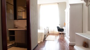 A bedroom with a bed, a desk, a chair, a window with curtains, and a bathroom with a sink and mirror. - Cocco e Dessì Home- Tamara (ORISTANO)
