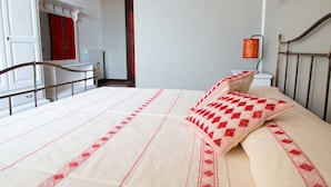 A bed with a patterned bedspread, a bedside table, a lamp, and a mirror. - Cocco e Dessì Home- Tamara (ORISTANO)