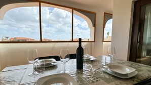 Une table à manger avec des assiettes, des verres et une bouteille, placée devant une fenêtre donnant sur des immeubles.