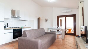 Une cuisine moderne avec des meubles blancs, un canapé gris et un coin repas comprenant une table et des chaises blanches.