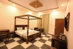 A hotel room with a four-poster bed, a desk, a chair, a TV, and a minibar. - The Van Bagh Ranthambore (Sawai Madhopur)