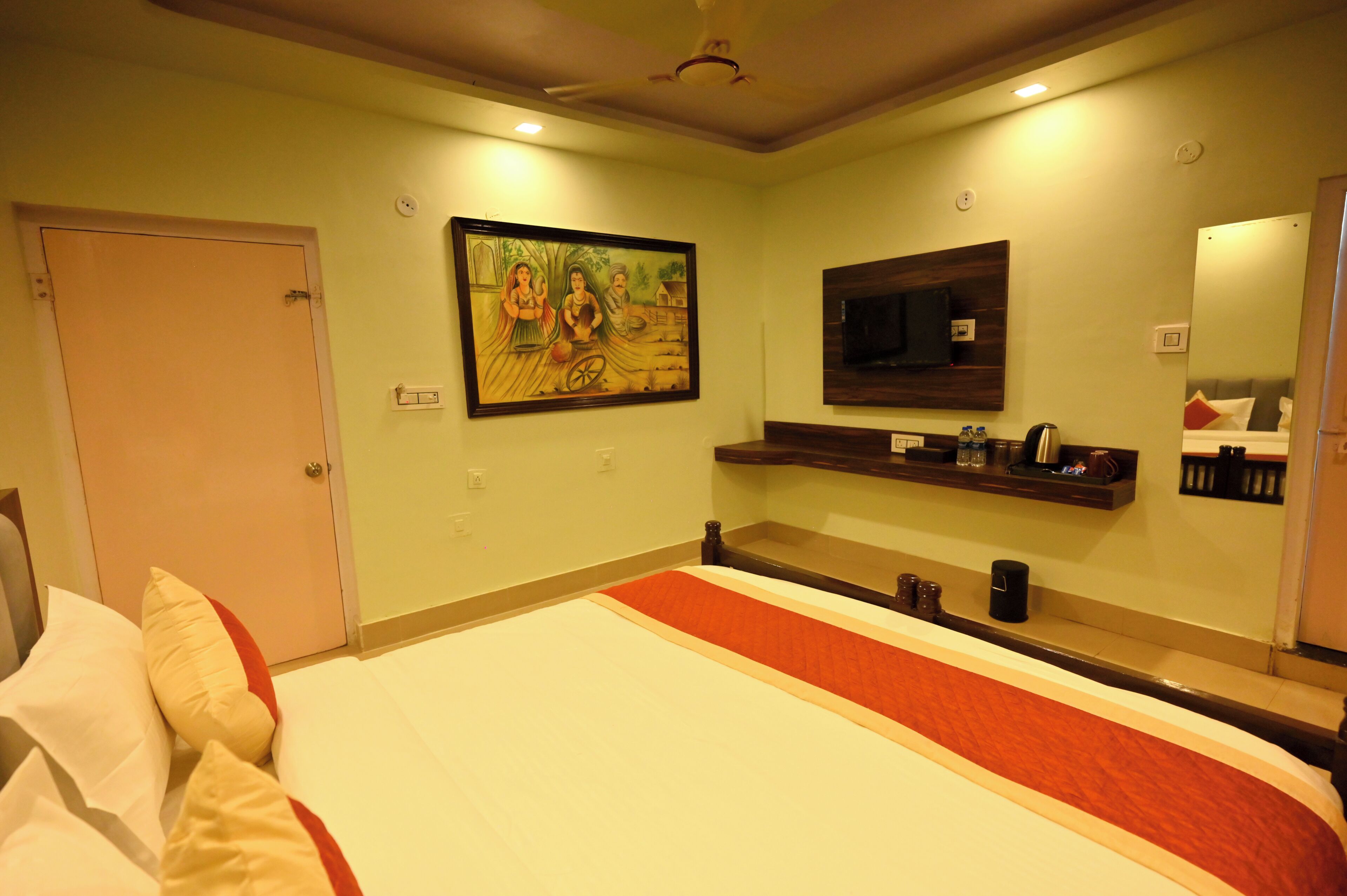 A hotel room with a bed, a painting on the wall, a TV, and a mirror.