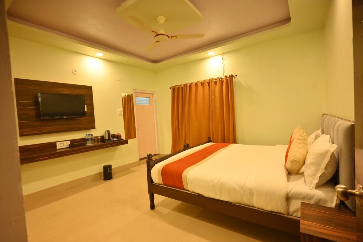 A neatly arranged bedroom with a bed, a mounted TV, a shelf with toiletries, and a door with a window.