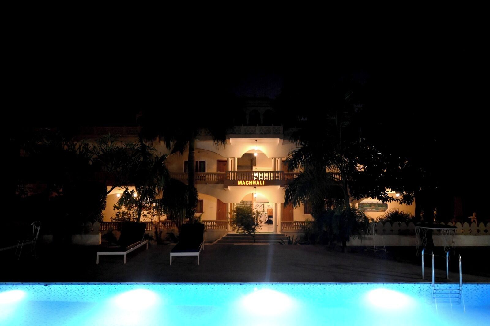 A hotel with a pool, a well-lit entrance, and a balcony.