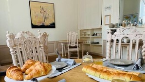 Een eettafel gedekt met brood, borden en een glas sap, in een kamer met sierlijke stoelen en een decoratieve spiegel.