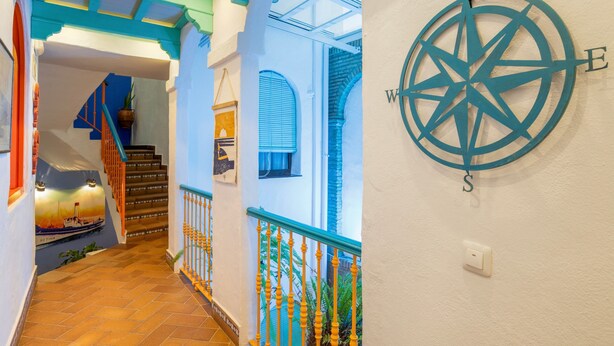 A staircase with a blue railing, a compass wall decoration, and a view of a boat through a window. - Room 'Hostal Santa Catalina 4' with Shared Terrace, Wi-Fi and Air Conditioning (Conil de la Frontera)