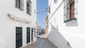 A narrow cobblestone street flanked by white buildings with barred windows and a clear blue sky. - Room 'Hostal Santa Catalina 4' with Shared Terrace, Wi-Fi and Air Conditioning (Conil de la Frontera)