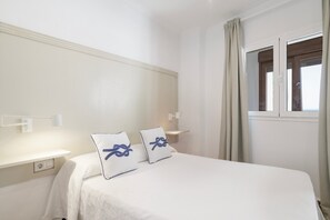 A hotel room with a bed, two pillows, a nightstand, a window with curtains, and a wall-mounted light. - Room 'Hostal Santa Catalina 8' with Shared Terrace, Wi-Fi & Air Conditioning (Conil de la Frontera)