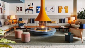 A modern living room with a central glass fireplace, striped sofas, and abstract wall art. - Near Newport Harbor + On-Site Dining. Pool. Bikes. (Newport)