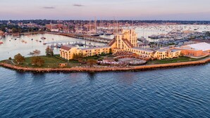 Un hotel frente al agua con varias construcciones, un puerto deportivo con numerosos barcos y una gran estructura central con techo a dos aguas.