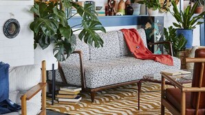 Una sala de estar acogedora con un sofá estampado, una mesa de centro de madera y diversas plantas.