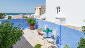 A rooftop terrace with a view of the sea, a castle in the background, and potted plants. - Room 'Hostal Santa Catalina 9' with Shared Terrace, Wi-Fi, and Air Conditioning (Conil de la Frontera)