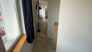 A narrow hallway with a window on the left, a floor lamp, and a wooden bench. - Le Chaleureux - Charmant T2 proche metro (Toulouse)