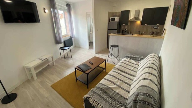 A modern living room with a sofa, coffee table, and a TV mounted on the wall. - Le Chaleureux - Charmant T2 proche metro (Toulouse)