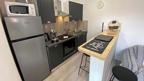 A compact kitchen with a refrigerator, microwave, stove, and a small dining area with stools. - Le Chaleureux - Charmant T2 proche metro (Toulouse)