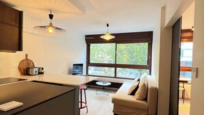 Cozinha moderna com ilha central, área de jantar com mesa redonda e um sofá perto de uma janela grande.