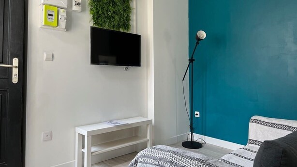 Slaapkamer met een muur in teal, een tv aan de muur bevestigd, een witte nachtkastje, een vloerlamp en een bed met beddengoed met een patroon.