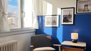 Une pièce avec une chaise, un radiateur, une table avec une lampe et des tableaux encadrés accrochés au mur.