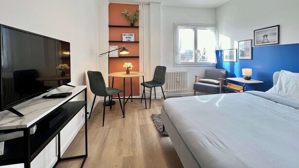 Une chambre d’hôtel moderne équipée d’un lit, d’un bureau, de chaises, d’une télévision et d’une fenêtre donnant sur la ville.