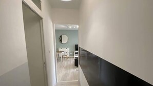 Un corridoio moderno con una porta a sinistra, una zona pranzo con tavolo e sedie al centro e un bancone nero a destra.