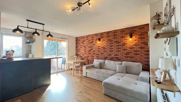 Ein modernes Wohnzimmer mit einer Ziegelfassade, einem grauen Ecksofa und einem Essbereich mit Tisch und Stühlen.